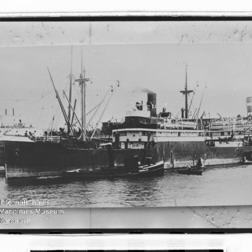 Historische Schwarzweißaufnahme eines großen Dampfschiffs im Hafen mit mehreren kleinen Booten daneben und Wasserzeichen 