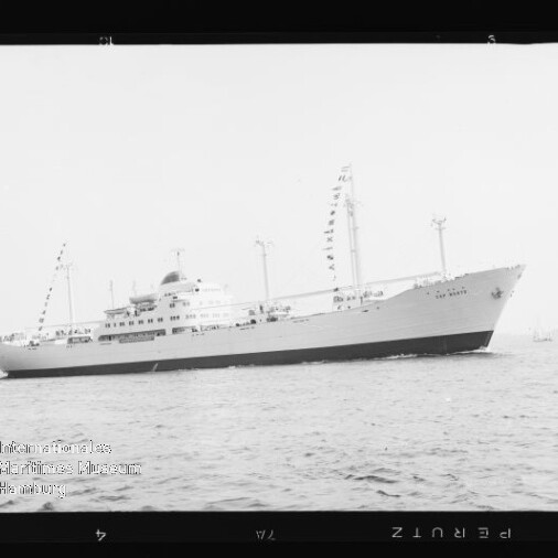 Weißes Passagierschiff mit Signalfahnen an mehreren Masten fährt über ruhige See, schwarz-weiß-Foto.