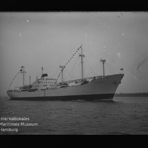 Großes Passagier- und Frachtschiff mit beflaggten Masten auf ruhigem Meer; Schwarzweißbild mit Museumslogo.
