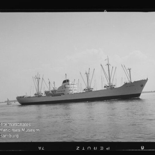 Seitliche Ansicht eines Frachtschiffs mit mehreren Ladekränen und Schornstein, auf ruhigem Wasser vor flachem Horizont.