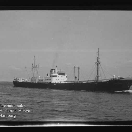 Schwarzweißaufnahme eines Frachtschiffs mit Ladekränen auf ruhiger See, mit Internationales Maritimes Museum Hamburg Wasserzeichen links unten.