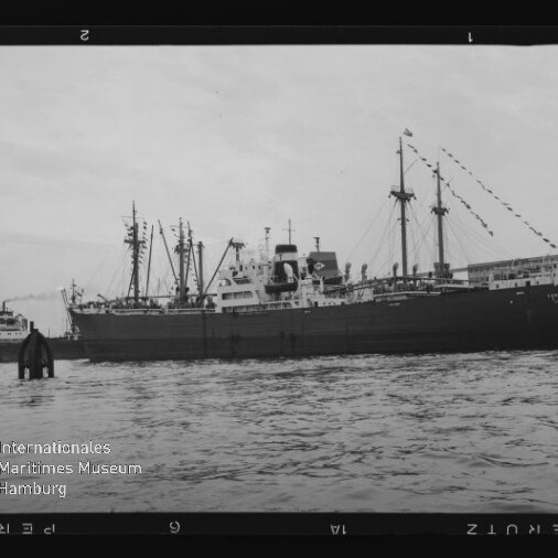 Schwarzweiß-Foto eines großen Frachtschiffs im Hafen, Wasser im Vordergrund und das Logo „Internationales Maritimes Museum Hamburg“.