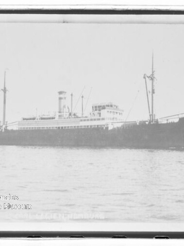 Großes dampfgetriebenes Frachtschiff mit Schornstein und Ladebäumen, seitliche Ansicht auf ruhiger See.