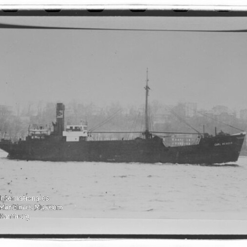 Seitliches Schwarz-Weiß-Bild eines Frachtschiffs auf ruhiger See mit Stadtsilhouette im Hintergrund und Museumswasserzeichen.