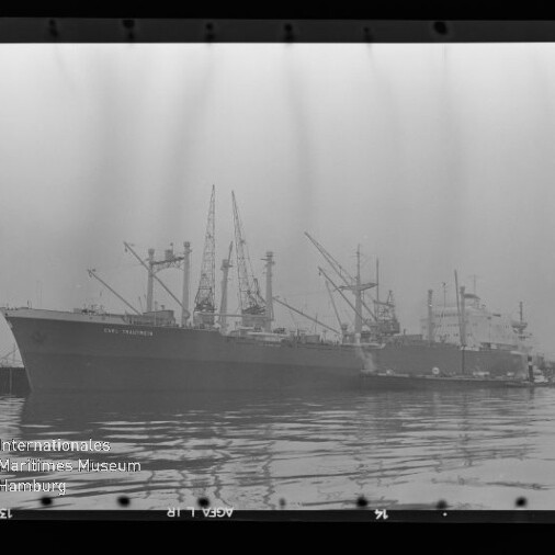 Großes Frachtschiff mit mehreren Ladekränen am Kai, ruhige Spiegelung im Wasser und Museumsstempel unten links.