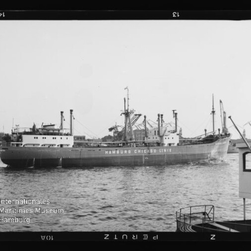 Schwarzweißfoto eines Frachtschiffs mit der Aufschrift HAMBURG CHICAGO LINE im Hafen, Kräne am Ufer.