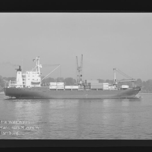Frachtschiff mit Containern und zwei Ladekränen fährt auf ruhigem Wasser vor Uferkulisse; Museumslogo unten links.