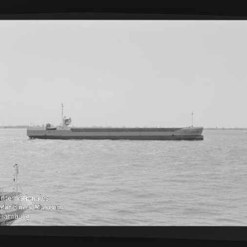 Langgestrecktes Frachtschiff mit Aufbauten achtern auf ruhiger See; Schwarzweißfoto mit Wasserzeichen 'Int. Maritimes Museum'
