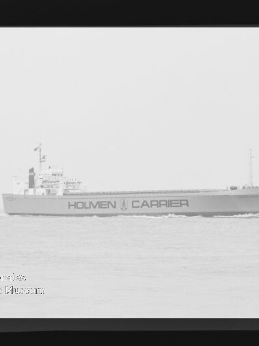 Seitenansicht eines Frachtschiffs mit der Aufschrift HOLMEN CARRIER, das ruhig auf dem Meer fährt.