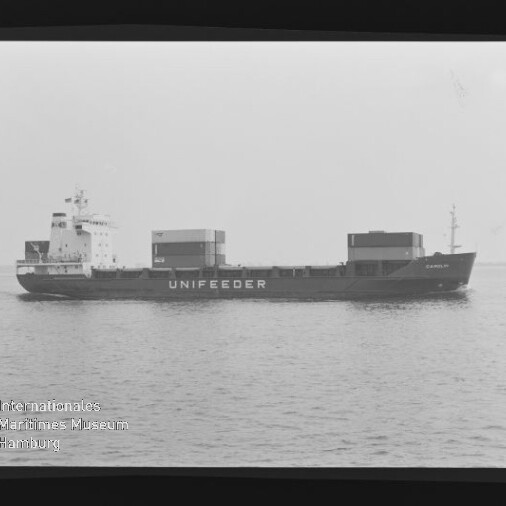 Schwarzweiß-Seitenansicht eines Frachtschiffs mit der Aufschrift UNIFEEDER und Containeraufbauten, ruhig auf See mit sichtbarem Filmrand.
