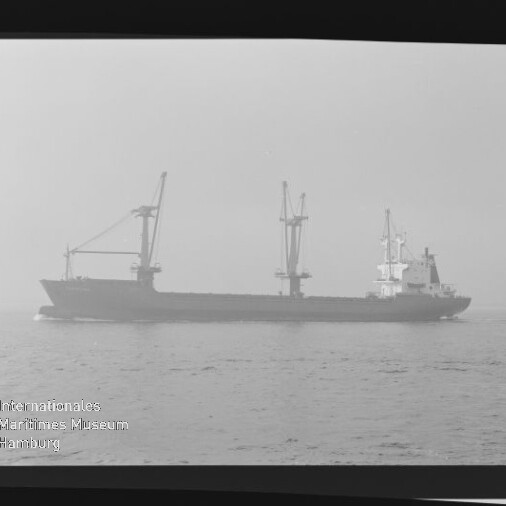 Frachtschiff mit drei Ladekränen als Nebelsilhouette auf ruhiger See, Filmrahmenrand sichtbar.