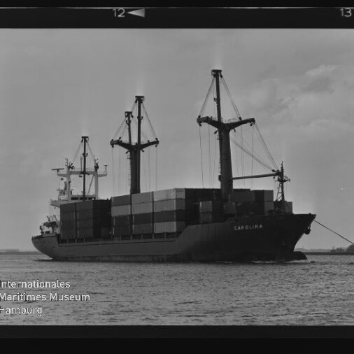Containerschiff CAROLINA mit gestapelten Containern und Ladekränen auf ruhigem Hafenwasser im schwarzweiß-Filmrahmen.