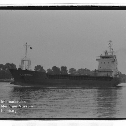 Frachtschiff A.A. Amsterdam auf ruhigem Wasser vor baumbestandener Uferlinie, Schwarzweißfoto