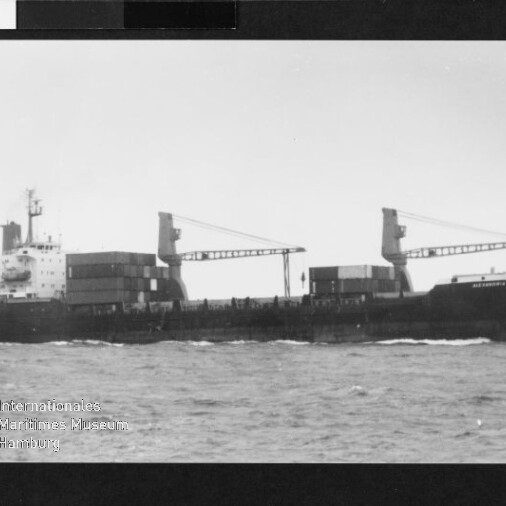 Frachtschiff mit zwei Ladekränen und gestapelten Containern auf offener See, Wasserzeichen des Internationalen Maritimen Museums Hamburg.