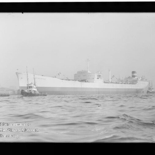 Großes Frachtschiff mit mehreren Schleppern im Hafen, Wellen im Vordergrund; Wasserzeichen 
