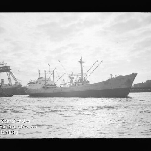 Frachtschiff im Hafen vor Hafenkränen, Wellen im Vordergrund; Textlogo Internationales Maritimes Museum Hamburg unten links