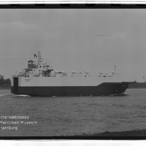 RoRo-Frachtschiff mit hellem Oberrumpf und dunklem Unterrumpf fährt auf einem Fluss; Museumslogo links unten.