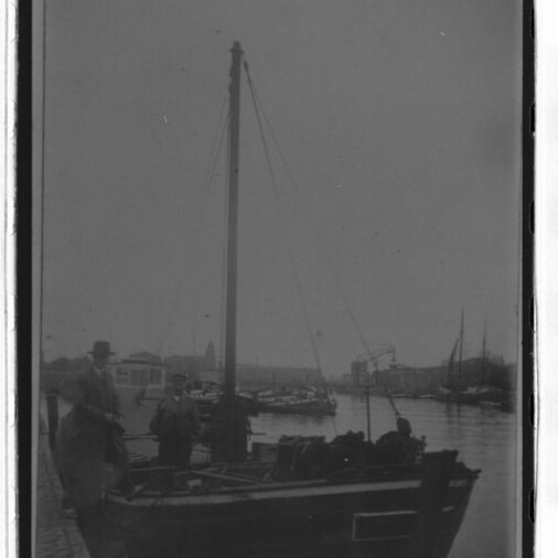 Kleines Segelboot am Kai mit zwei Personen, düstere Hafenkulisse und sichtbares Logo Internationales Maritimes Museum Hamburg