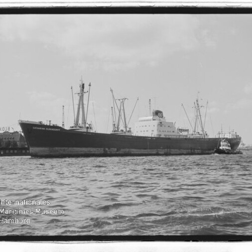 Großes Frachtschiff am Kai mit Hafenkränen im Hintergrund, zwei Schlepper auf dem Wasser und Museumslogo links unten.