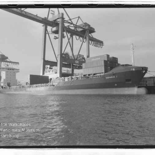 Frachtschiff am Kai mit Containern und Hafenkranen; Siegel des Internationalen Maritimen Museums Hamburg sichtbar.