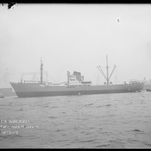 Frachtschiff im Hafen vor Krananlagen, leicht neblige Sicht; Schriftzug Internationales Maritimes Museum Hamburg unten links.