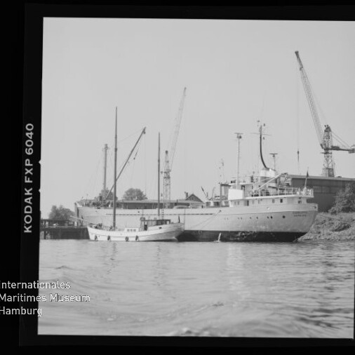 Großes und kleines Schiff am Kai vor mehreren Hafenkränen, ruhige Wasserfläche und sichtbarer Kodak-Filmrand