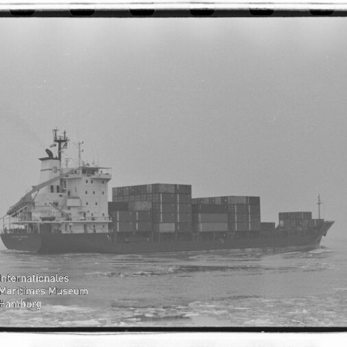 Frachtschiff mit aufgetürmten Containern fährt auf ruhiger See; schwarz-weiß-Aufnahme mit Wasserzeichen des Internationalen Maritimen Museums Hamburg.