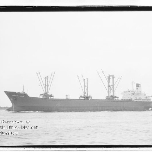 Frachtschiff mit drei Ladekränen und weißen Aufbauten achtern auf ruhiger See; Museumsstempel unten links.