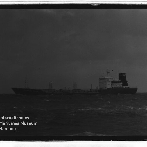 Frachtschiff mit Aufbauten achtern auf rauer See unter dunklem Himmel; links unten Wasserzeichen Maritimes Museum Hamburg.