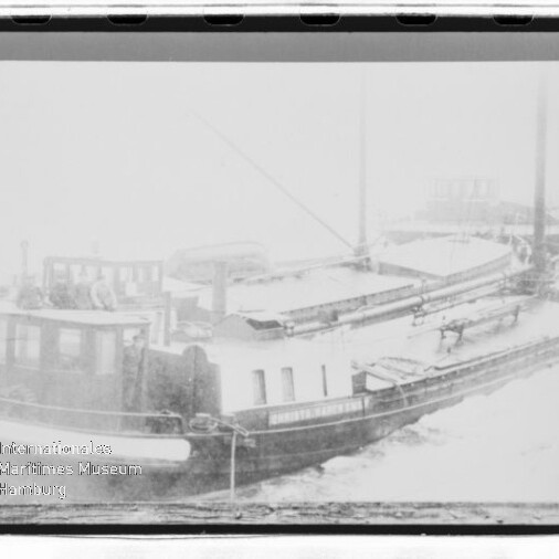 Schneebedeckter Lastkahn im Hafen mit Steuerhaus und flachem Laderaum, unten links Wasserzeichen eines Maritimen Museums.