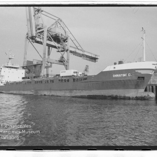 Frachtschiff CHRISTINE C. am Industriequai neben großem Hafenkran, im Vordergrund Wasser.