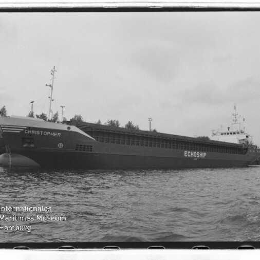 Schwarzweißfoto eines Frachtschiffs mit Namen CHRISTOPHER und Schriftzug ECHOSHIP, längsseits am Kai, Wasser im Vordergrund.
