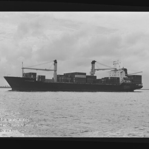 Schwarzweiß-Seitenansicht eines Containerschiffs mit Deckskranen und Containern auf ruhiger See, Museumswasserzeichen links unten.