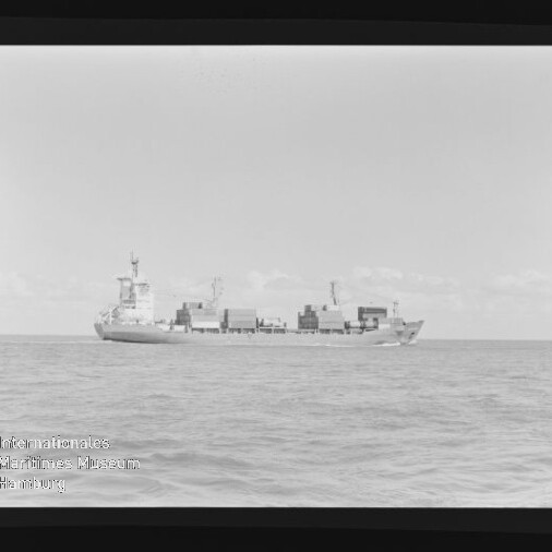 Schwarzweiß-Foto eines Containerschiffs mit gestapelten Containern auf ruhiger See, Filmrand und Museumswasserzeichen.