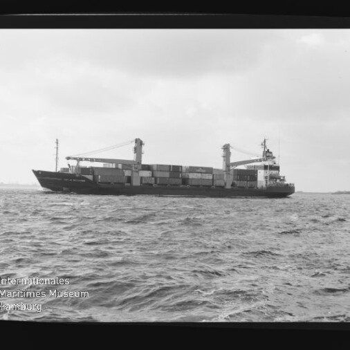 Containerschiff mit aufgestapelten Containern und zwei Ladekränen auf rauer See unter bewölktem Himmel.