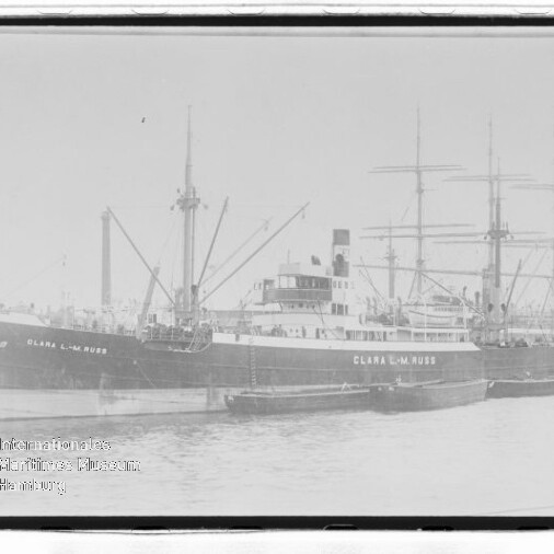 Schwarzweißaufnahme eines am Kai liegenden Frachtschiffs CLARA L.M. RUSS mit Masten, Ladebaum und Beiboot.