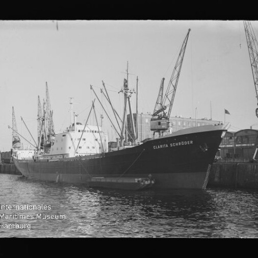 Frachtschiff Clarita Schröder am Kai eines Industriehafens, mehrere Hafenkräne im Hintergrund.