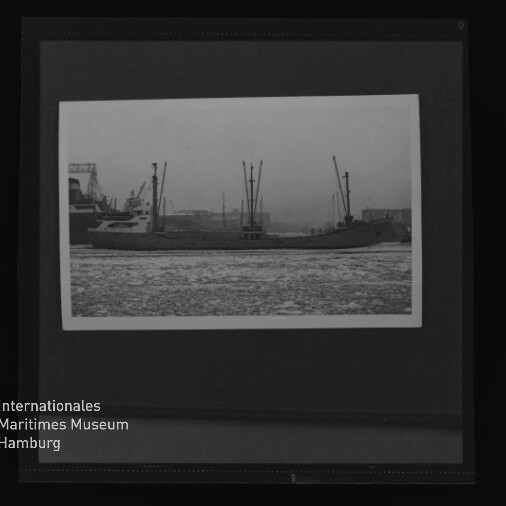 Schwarzweißfoto eines Frachtschiffs mit mehreren Ladekränen im Hafen, im Vordergrund vereistes Wasser und Museumslogo