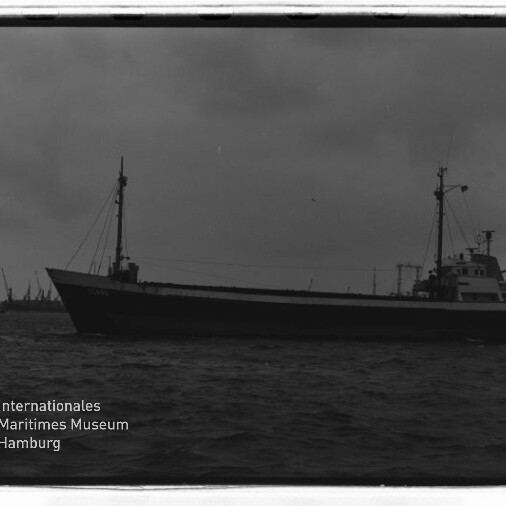 Schwarzweißfoto eines Frachtschiffs im Hafen vor Kranreihe; Logo des Internationalen Maritimen Museums Hamburg links unten