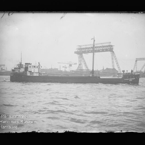 Schwarzweißfoto: Frachtschiff auf dem Wasser vor großen Hafenkränen; Wasserzeichen des Internationalen Maritimen Museums Hamburg.