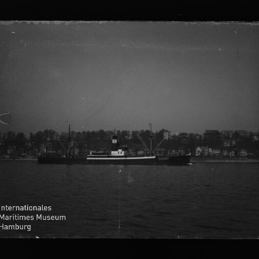 Schwarzweißfoto eines Frachtschiffs auf ruhigem Wasser vor Ufer mit Häusern; Schriftzug 'Maritimes Museum Hamburg' links unten.