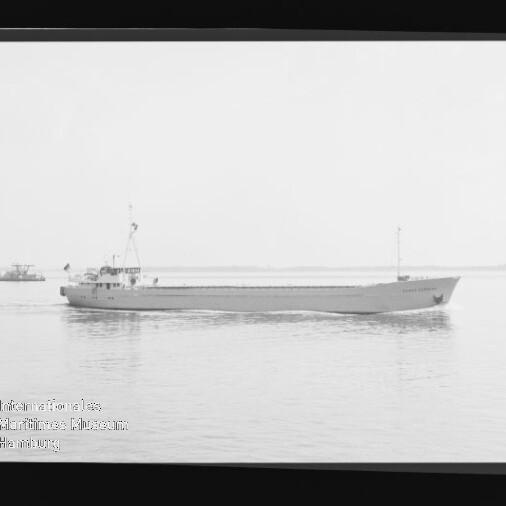 Seitliche Aufnahme eines Frachtschiffs auf ruhigem Wasser in Schwarzweiß, kleines Beiboot am Horizont und Museums-Wasserzeichen links unten.