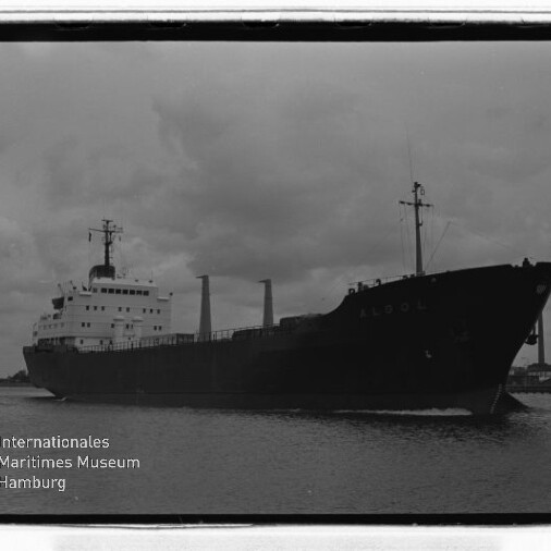 Großes Frachtschiff im Hafen unter bewölktem Himmel, Krananlagen am Ufer, Schwarzweißfoto mit Museumslogo.