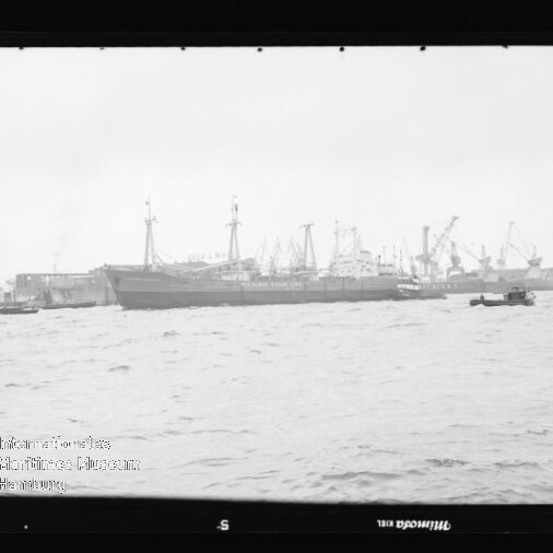 Frachtschiff am Hafen mit mehreren Kranen und einem kleinen Boot im Vordergrund, Schwarzweißaufnahme