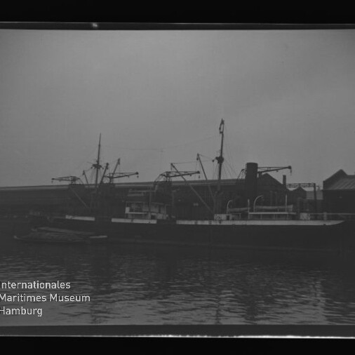 Schwarzweißfoto eines Frachtschiffs am Kai mit Kränen und Lagerhalle; Wasserzeichen Maritimes Museum Hamburg