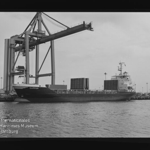 Frachtschiff CLIPPER am Kai unter einem großen Container-Kran, mehrere Container an Deck und Wasser im Vordergrund.
