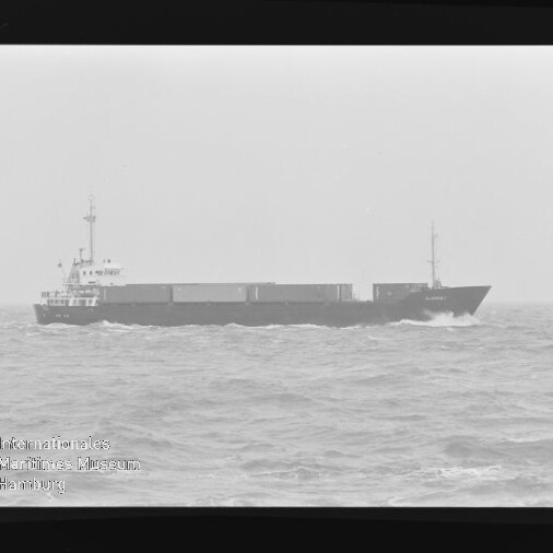 Schwarzweiß-Aufnahme eines Containerschiffs auf bewegter See, Filmrahmen und Museumslogo unten links sichtbar.