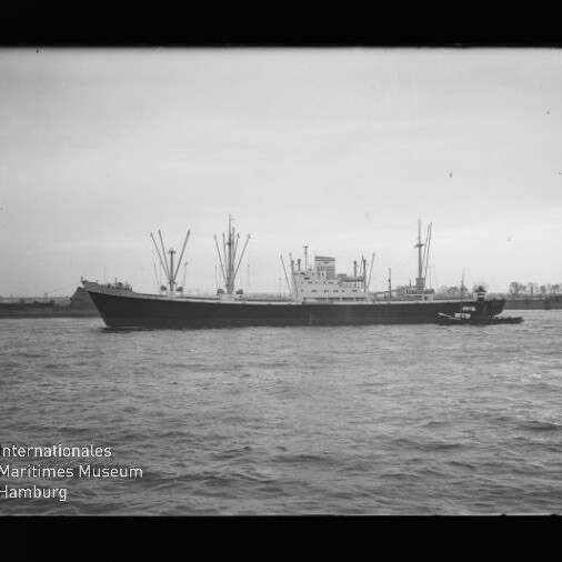 Frachtschiff mit Ladekränen und einem Schlepper an der Seite auf Wasser, mit sichtbarem Museumssignet.