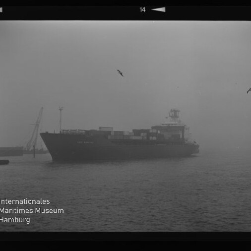 Containerschiff fährt durch dichten Nebel im Hafen, Container auf Deck, Möwen am Himmel und Museumslogo links unten