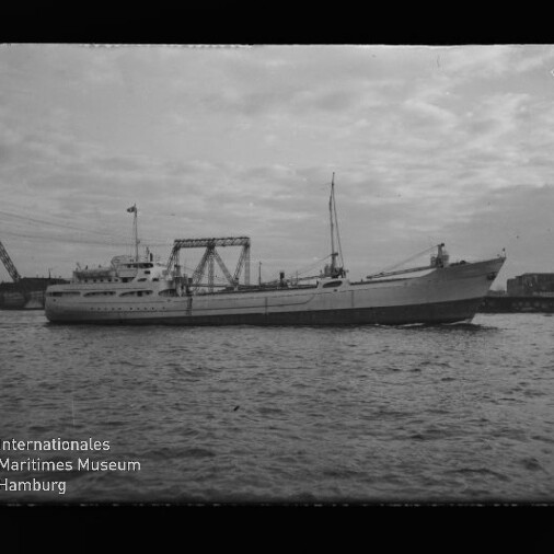 Schwarzweißbild eines Frachtschiffs in Hafen, Seitenansicht vor Krananlagen, mit Museumswasserzeichen unten links.